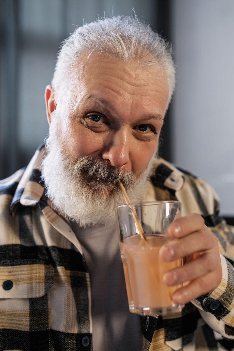 Starší muž s šedivým vousem pije smoothie brčkem
