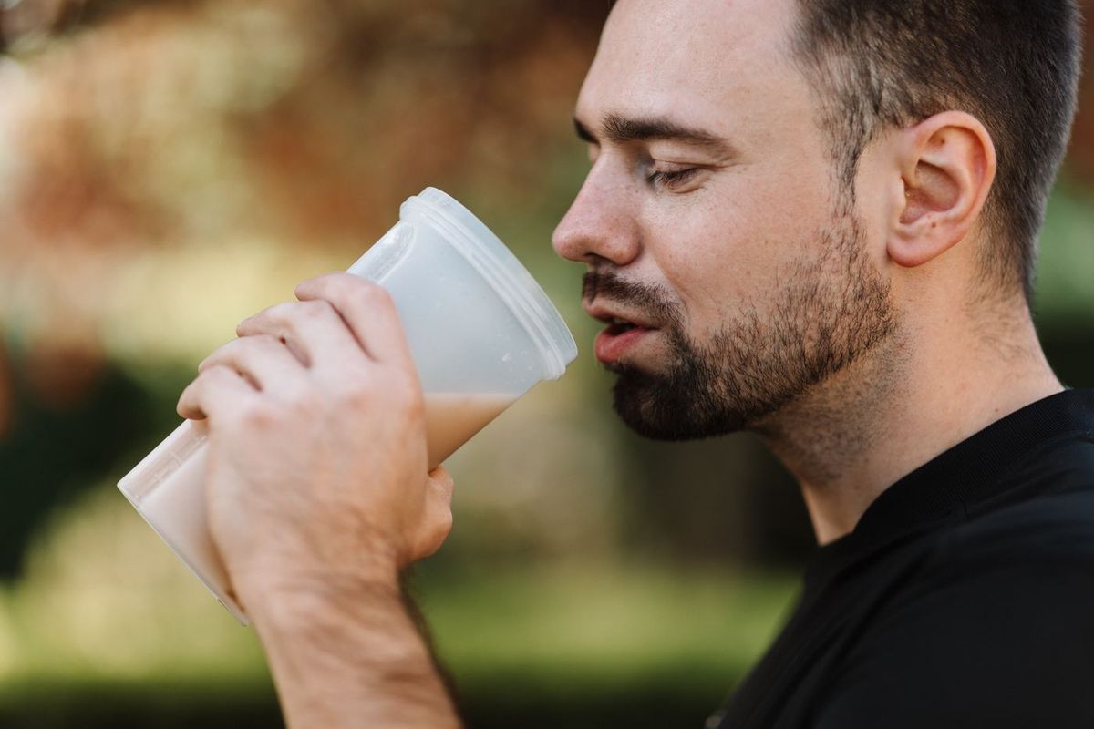 Muž s plnovousem pije venku smoothie z kelímku